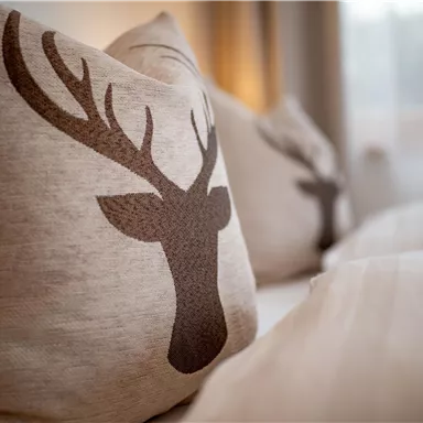 A pillow with a stylized reindeer antler pattern. The colors are neutral and warm, creating a cozy atmosphere.