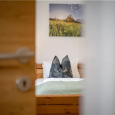 A cozy bedroom with a bed and decorative pillows. A beautifully designed picture of a landscape hangs on the wall.