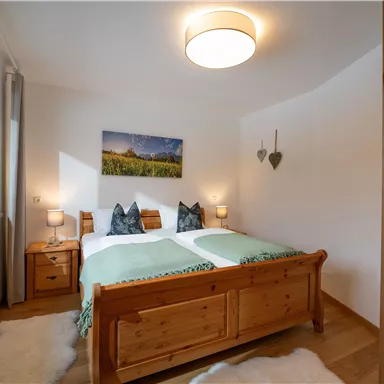 A cozy bedroom with a wooden double bed and two nightstands. Hearts and a landscape picture hang on the walls.