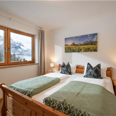 A cozy bedroom with two beds and wooden furniture. Large windows offer a beautiful view of the mountains.