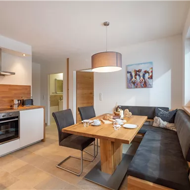 A modern kitchen with a dining area and a wooden table. The decor is bright and friendly, ideal for social gatherings.