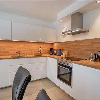 A modern kitchen with bright cabinets and wood surfaces. It is well equipped with appliances such as a stove, a coffee machine, and a kettle.