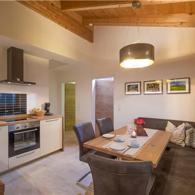 A modern kitchen with a dining area and a large table. The room has wood accents and large windows that provide plenty of light.