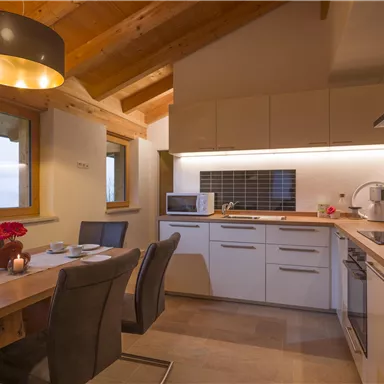 A modern kitchen with a wooden ceiling and a large dining table. The atmosphere is warm and inviting, with windows that let in plenty of daylight.