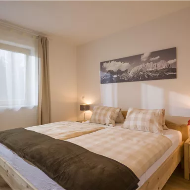 A cozy bedroom with a double bed, bright walls, and large windows. The decor is modern and inviting, perfect for a relaxing stay.