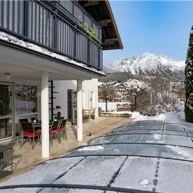A modern terrace with seating, surrounded by snow and overlooking the mountains. The clear sky gives the winter landscape a fresh atmosphere.