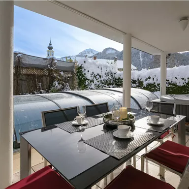 A beautiful outdoor area with a modern table and red chairs. In the background, snow-covered mountains and a clear blue sky can be seen.