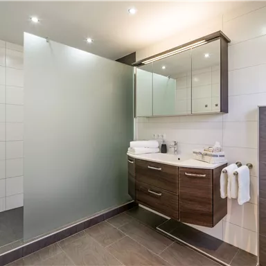 A modern bathroom with a glass shower and a simple sink. It is bright and minimally designed.