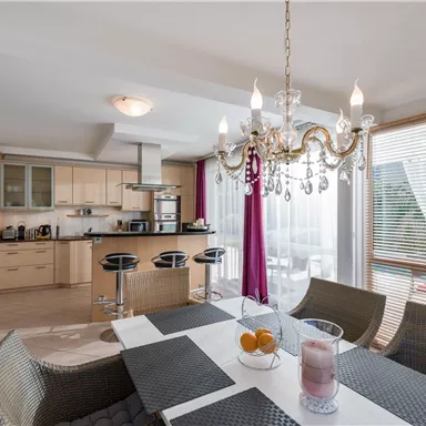 A modern kitchen with a dining area. The light from a chandelier creates an inviting atmosphere.