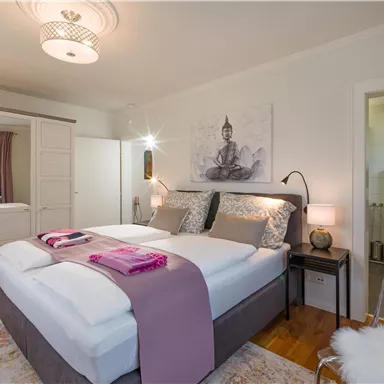 A cozy bedroom with a double bed, a piece of art above the bed, and modern furniture. The room is bright and inviting, with a warm wooden floor and coordinated textiles.