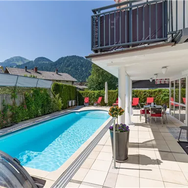 A modern house with a swimming pool and cozy seating areas. The surroundings are surrounded by mountains and lots of greenery.