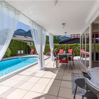 A modern terrace overlooking a pool. The area is furnished with elegant furniture and green plants.