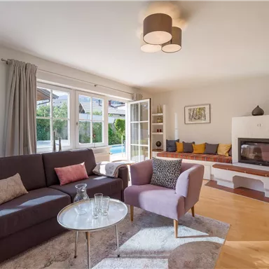 A modern living room with a comfortable sofa and an elegant table. Large windows provide plenty of daylight and a view of the garden.
