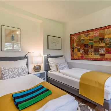 A cozy bedroom with two single beds and colorful blankets. On the wall hangs a colorful wall tapestry that gives the room a warm atmosphere.