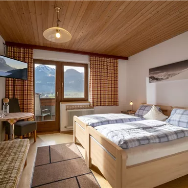 Ein gemütliches Schlafzimmer mit zwei Einzelbetten und einer warmen Holzdecke. Der Raum hat ein Fenster mit Blick auf die Berge und einen kleinen Tisch.