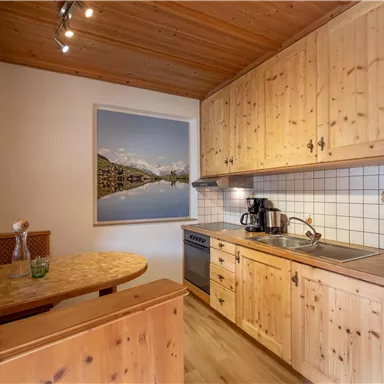 Eine gemütliche Küche mit Holzmöbeln und einer kleinen Essecke. An der Wand hängt ein Bild einer Berglandschaft.