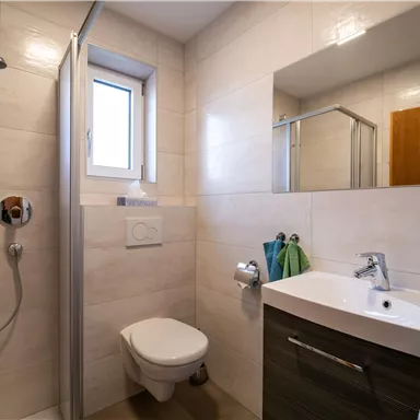 Ein modernes Badezimmer mit einer Dusche und einem Waschbecken. Helle Fliesen und große Spiegelflächen sorgen für eine freundliche Atmosphäre.