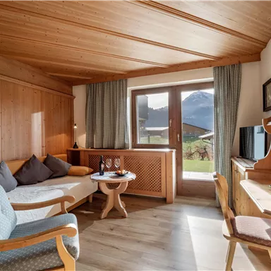 Ein gemütliches Zimmer mit Holzverkleidung und einem schönen Ausblick auf die Berge. Es gibt eine Sitzecke, einen Tisch und einen Arbeitsplatz.