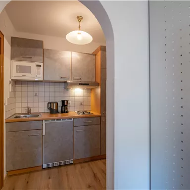 Eine moderne Küche mit Holzoberflächen und weißen Wänden. Sie ist gut ausgestattet mit einem Herd, einer Mikrowelle und weiteren Geräten.