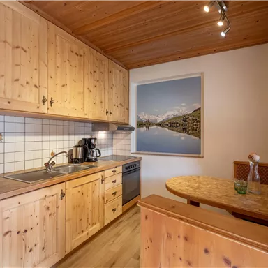 Eine gemütliche Küche aus hellem Holz mit modernen Geräten. Es gibt einen Esstisch und ein Bild mit Berglandschaft an der Wand.