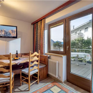 Ein gemütlicher Essbereich mit einem Tisch und Stühlen. Durch das Fenster ist ein Balkon mit Blick auf die Umgebung zu sehen.