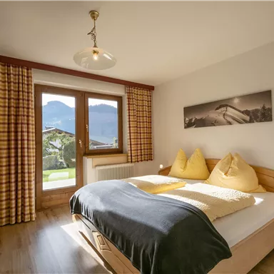 Ein helles Schlafzimmer mit einem Doppelbett und zwei Kissen in Form von Spitzen. Große Fenster bieten einen schönen Blick auf die Berge und frisches Tageslicht.