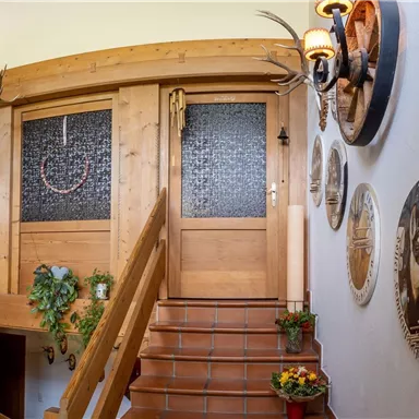 Ein einladender Flur mit einer Holztreppe und dekorativen Wandtellern. An den Wänden hängen Jagdtrophäen und malerische Bilder von Tieren.