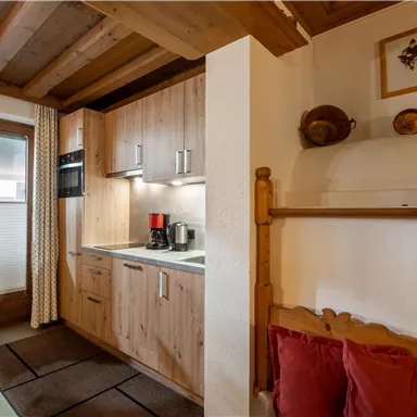 Eine gemütliche Küchenzeile aus Holz mit modernen Geräten. Daneben befindet sich ein rustikales Bett mit roten Kissen.