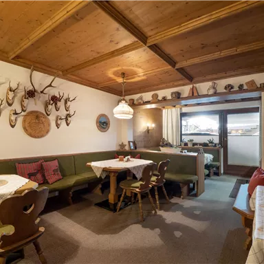 Ein gemütliches Restaurant mit Holzmöbeln und traditioneller Dekoration. Die Wände sind mit Geweihen geschmückt, und es gibt Tischdecken auf den Tischen.