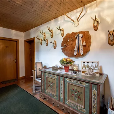 Ein einladender Flur mit Holzdecke und stilvollem Möbelstück. An den Wänden hängen Geweihstücke sowie eine dekorative Holztafel.