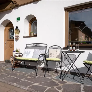 A cozy terrace with an entrance and a small table. There are two colorful benches and a friendly, inviting atmosphere.