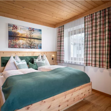 A cozy bedroom with a double bed and wood paneling. The room has a window with curtains and a picture on the wall.