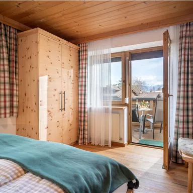 A cozy bedroom with a wooden ceiling and checked curtains. The balcony offers a view of the surroundings and fresh air.