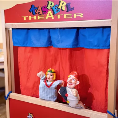 A puppet theater with colorful puppets is on a table. The puppets depict a Kasper and a girl who are waiting for a performance.
