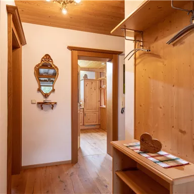 A cozy entrance area with wooden walls and a mirror. The floor is made of wood, and a small table stands next to a coat rack.