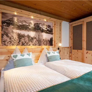 A cozy bedroom with two single beds and wooden paneling. A picture of mountains hangs on the wall, and the bed linen has a checked pattern.