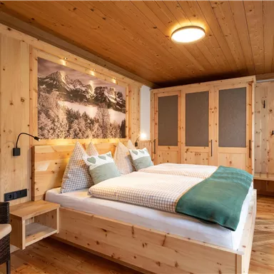 A cozy room with wooden paneling and a double bed. The room is bright and friendly, with a beautiful view of the mountains.