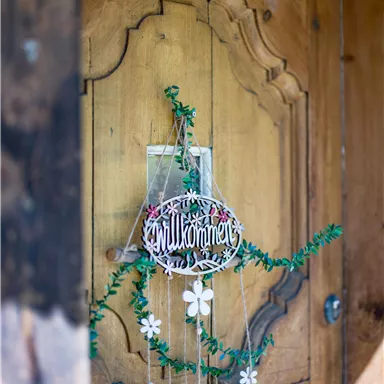 A beautiful wooden door with a welcome sign and decorative flowers. The door has a rustic design and is framed by a green garland.