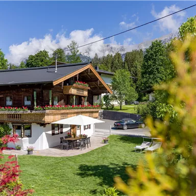 A cozy house with a balcony and a garden. The surroundings are green and idyllic, surrounded by trees and flowers.
