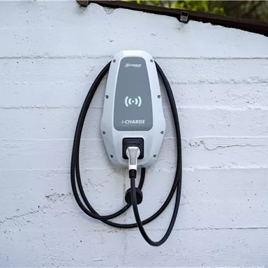 A modern electric car charging station is mounted on a wall. The charging station has two cables and a simple, elegant design.
