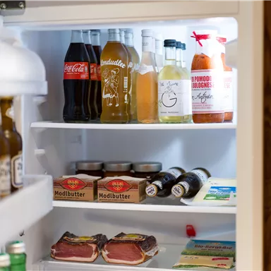 A refrigerator filled with various drinks and foods. Among other things, cola, meat, and Modl butter are visible.