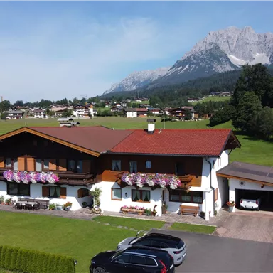 Ein schönes Haus im ländlichen Gebiet, umgeben von grünen Wiesen und Bergen im Hintergrund. Die Fassade des Hauses ist mit Blumen geschmückt.