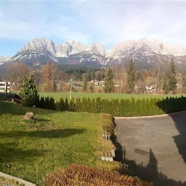 A picturesque landscape with majestic mountains in the background. In the foreground, there is green grass and a paved path.