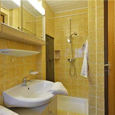 A modern bathroom with yellow tiles. There is a sink, a shower, and a mirror.