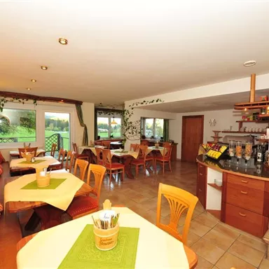 A cozy restaurant with bright tables and chairs. Large windows offer a view of the greenery.