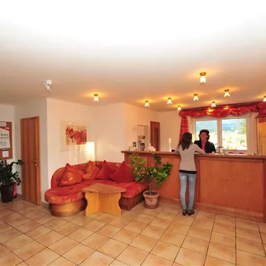 A reception area with a large couch and a wooden desk. There are plants and warm light, creating an inviting atmosphere.