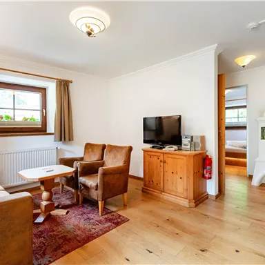 Ein gemütlicher Wohnbereich mit zwei Sesseln und einem Tisch. An der Wand befindet sich ein Fernseher und ein Fenster mit Blick nach draußen.