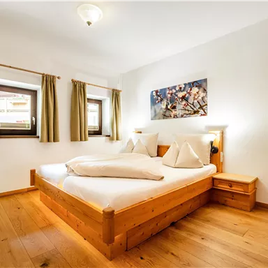 Ein gemütliches Schlafzimmer mit einem Doppelbett und Holzfußboden. Die Wände sind hell, und es gibt Fenster mit grünen Vorhängen.