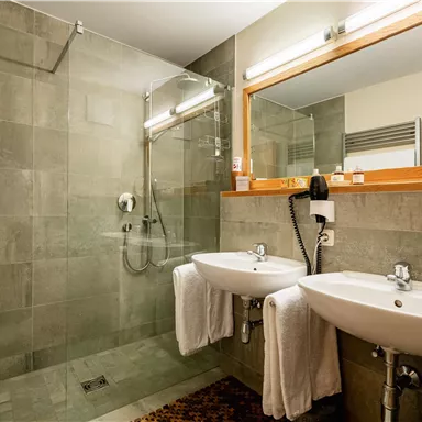 Ein modernes Badezimmer mit zwei Waschbecken und einer ebenerdigen Dusche. Die Wände sind in grauen Tönen gehalten und es gibt handtücher.