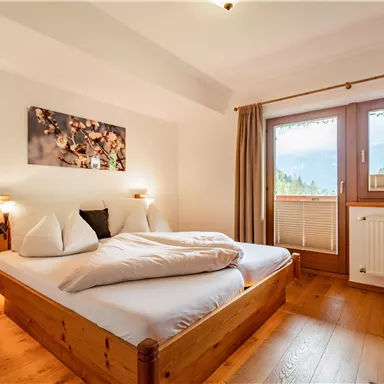 Ein gemütliches Schlafzimmer mit einem großen Doppelbett und Holzmöbeln. Große Fenster lassen viel Licht herein und bieten einen Blick auf die Natur.